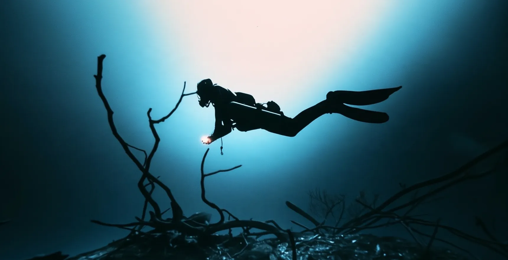A diver in silhouette against the turquoise glow of a Tulum cenote