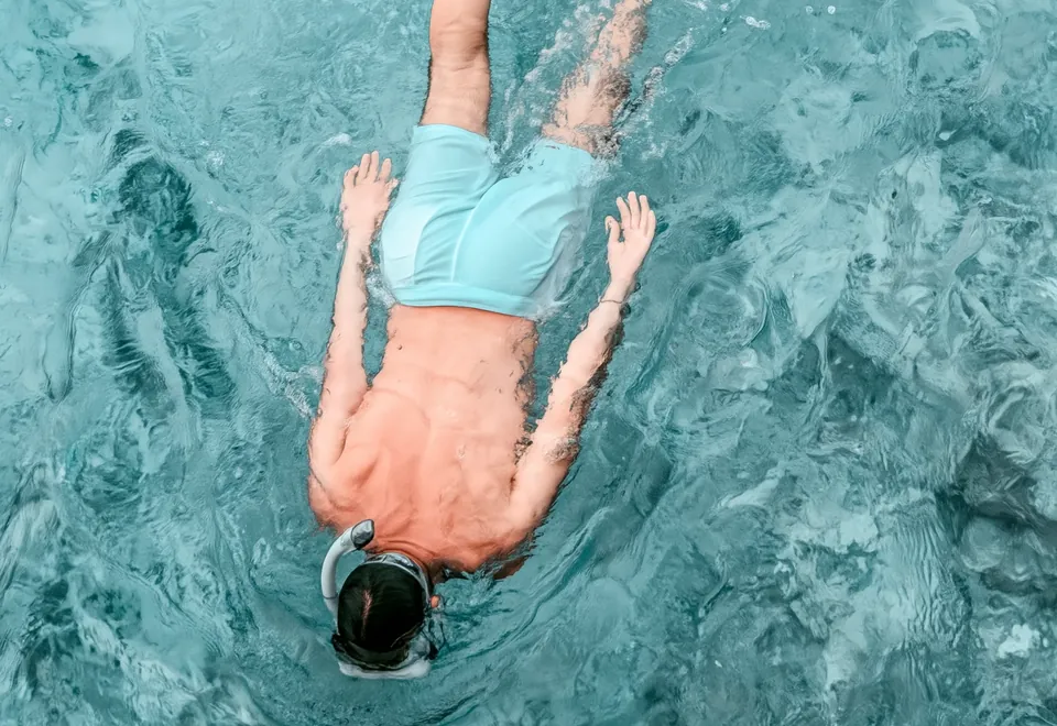 A snorkeller seen from above, mask and fins on, in turquoise water