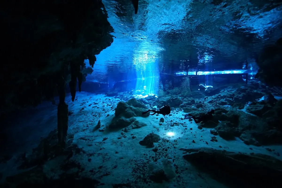 Divers in the cavern at Dos Ojos, daylight piercing the blue water