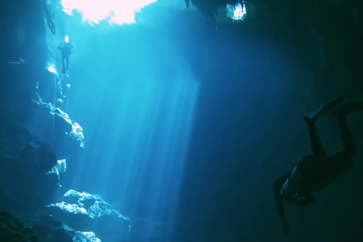 Shafts of light dropping down the well of El Pit, divers in silhouette